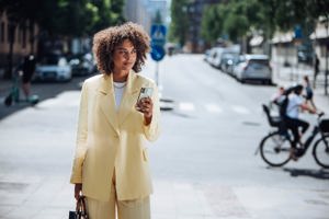 kvinna står mitt på en väg och kollar ut på gatan och håller i en telefon