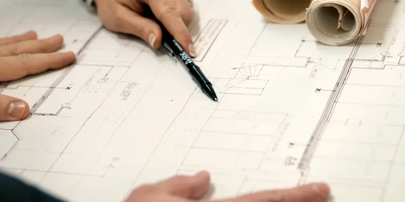 Två par händer granskar byggnadsritningar som ligger på ett bord