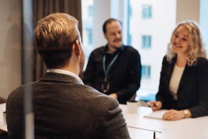 Tre personer sitter vid ett bord och pratar och ler med en kopp och anteckningsblock