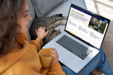 Kvinna sitter i soffan tillsammans med en katt och sin laptop i knät